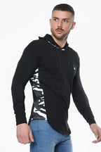 A man wears a black Prestige Camo Hooded Tee featuring white and grey camouflage side panels and full sleeves.